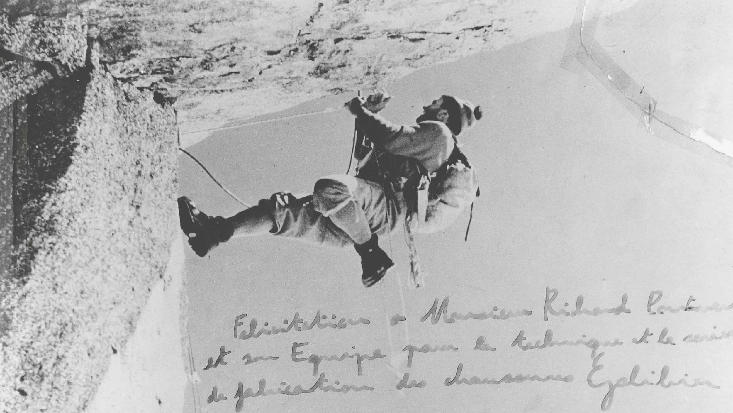 Photographie d'archive de l'alpiniste Lionel Terray en plein rappel sur une paroi rocheuse. L'image comporte une dédicace manuscrite remerciant Monsieur Richard-Pontvert et son équipe pour la technique de fabrication des chaussures Galibier.