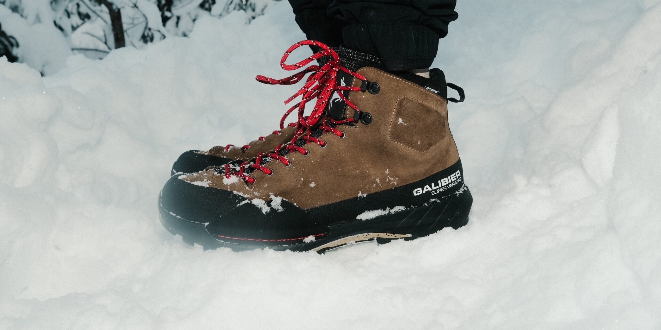 Gros plan sur une chaussure de randonnée marron, avec le logo Sympatex visible et des lacets rouges.