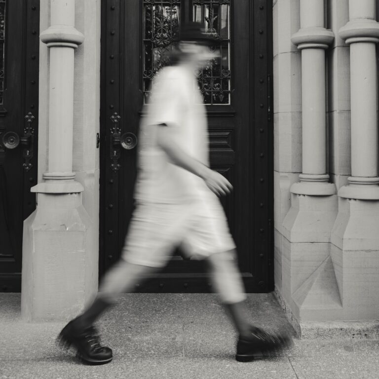 Silhouette floue d'un marcheur urbain portant des chaussures Galibier, marchant devant une porte.