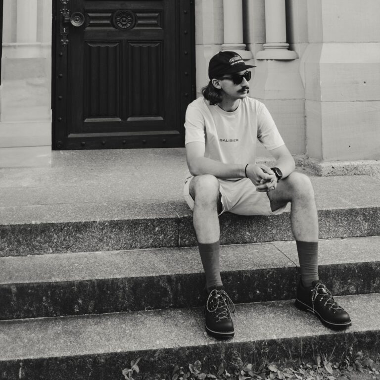 Homme assis portant des chaussures de marche urbaine Galibier en cuir noir avec lacets rouges et chaussettes rouges, style urbain décontracté.