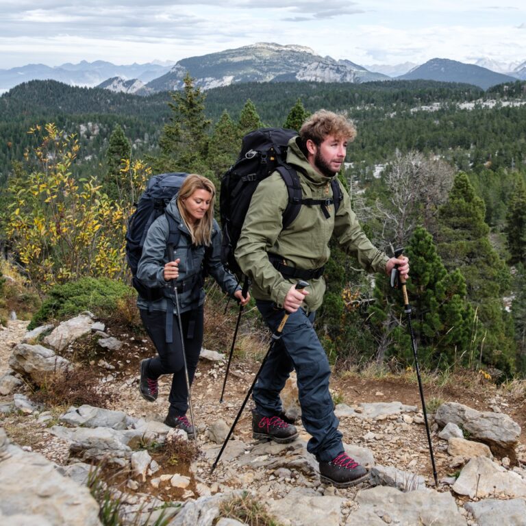 Un homme et une femme équipés de sacs à dos volumineux descendent un sentier de montagne technique et pierreux à l'aide de bâtons. chaussure trekking homme