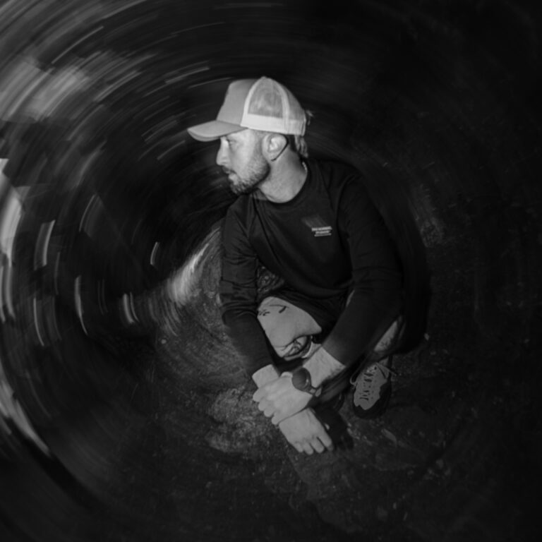 Portrait en noir et blanc d'un marcheur de fast hiking accroupi en forêt avec un effet de mouvement circulaire.