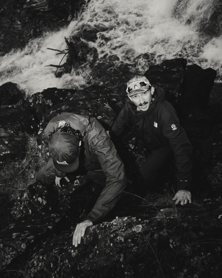 Vue d'en haut en noir et blanc de deux hommes grimpant une paroi rocheuse escarpée près d'un torrent.