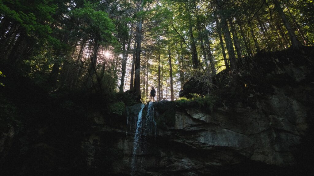 Silhouette d'un randonneur pratiquant le fast hiking et le speed hiking au sommet d'une cascade en forêt de montagne.