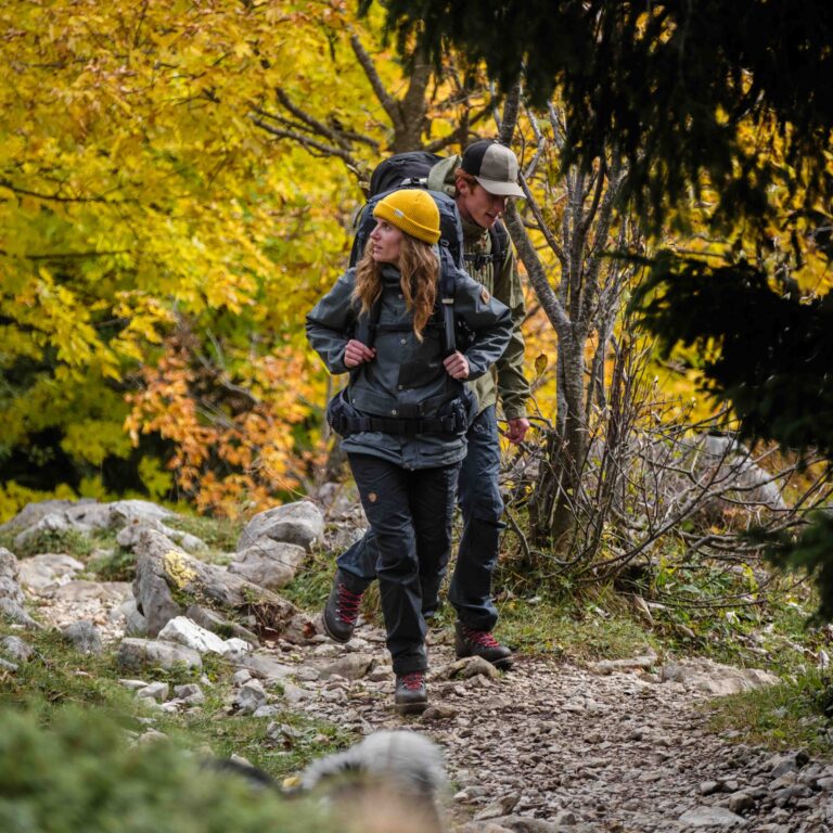 Couple de randonneurs en marche active sur un sentier de montagne rocailleux entouré d'arbres d'automne.