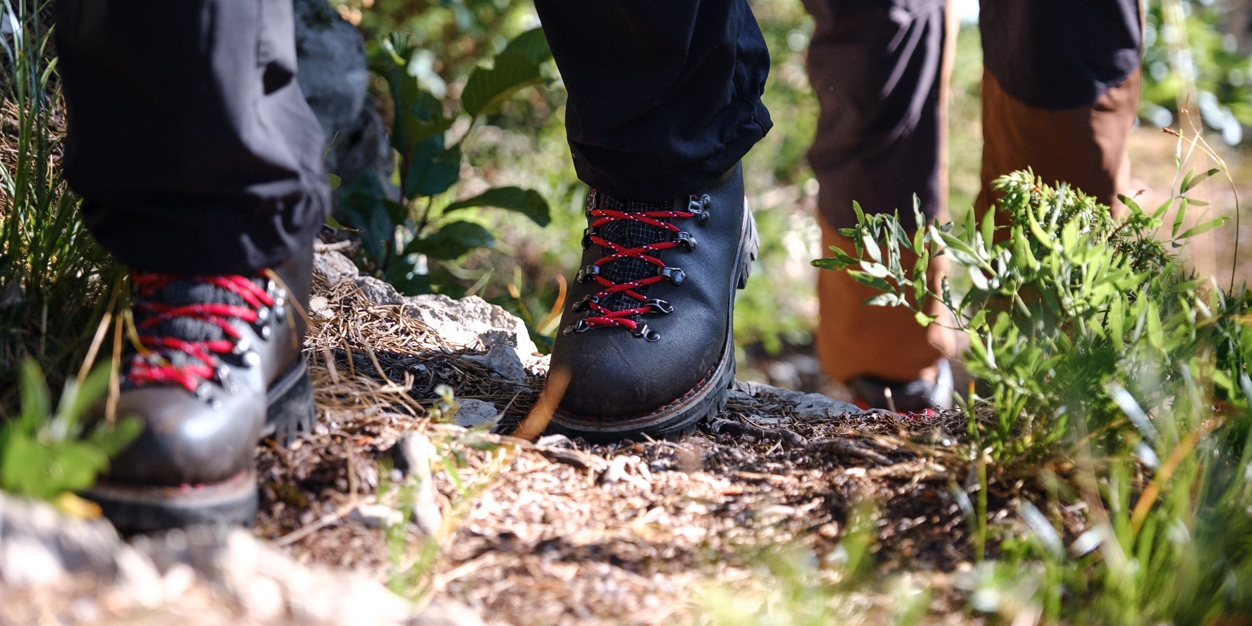 Gros plan sur des chaussures de randonnée en cuir brun Galibier avec lacets rouges sur un sentier rocailleux.