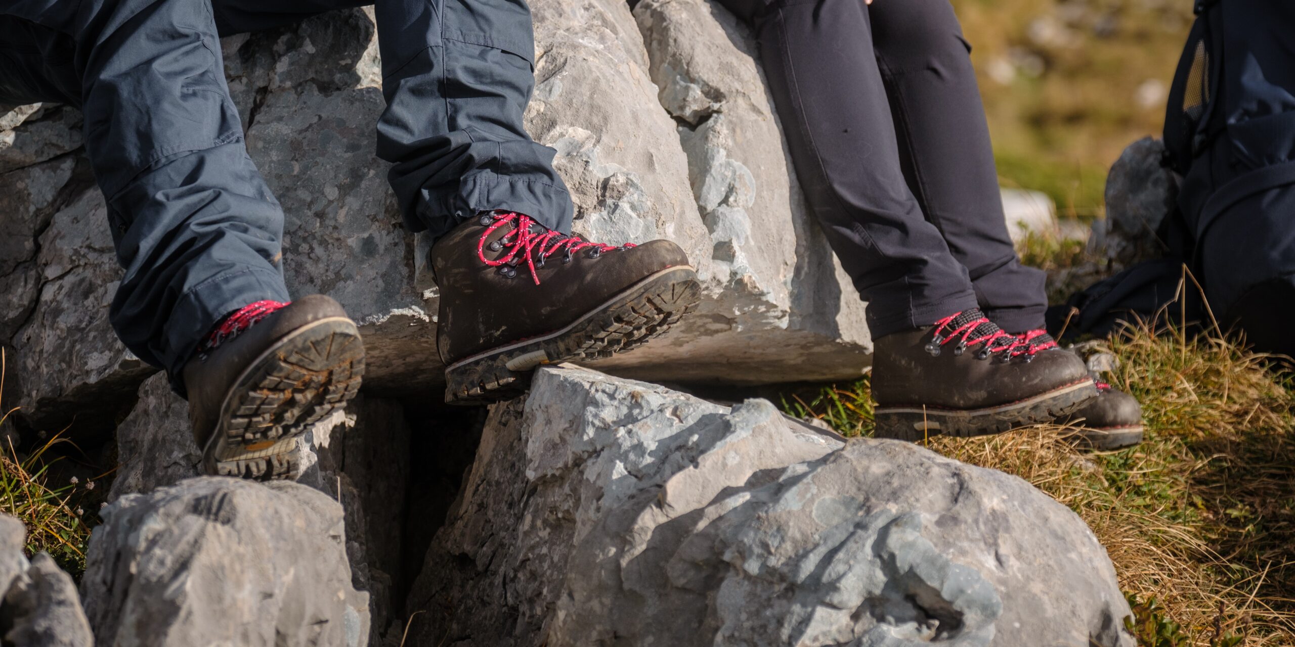 Gros plan sur deux paires de chaussures de trekking en cuir Galibier avec lacets rouges, posées sur des blocs de rochers en montagne pour la pratique de la randonnée en montagne.
