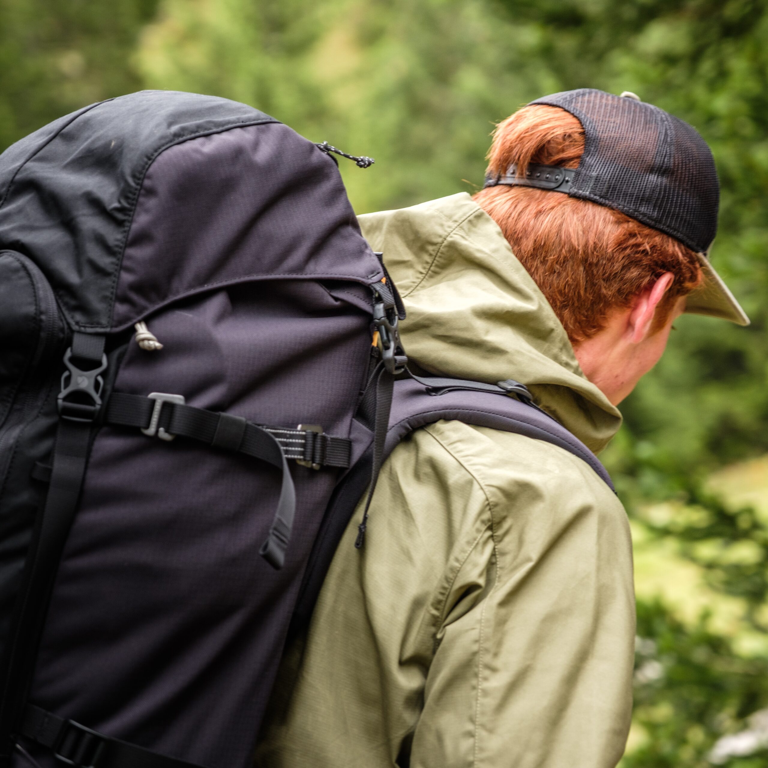 Vue rapprochée de profil d'un randonneur portant un grand sac à dos de trek noir Fjällräven et une veste technique olive.