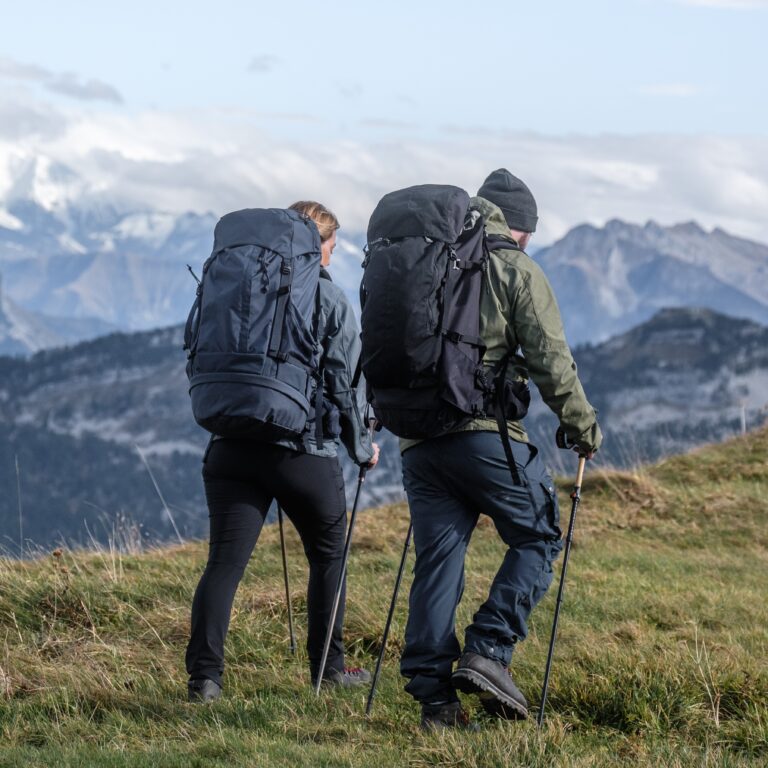 Deux marcheurs avec sacs à dos de randonnée itinérante descendent une pente herbeuse en montagne à l'aide de bâtons de marche.