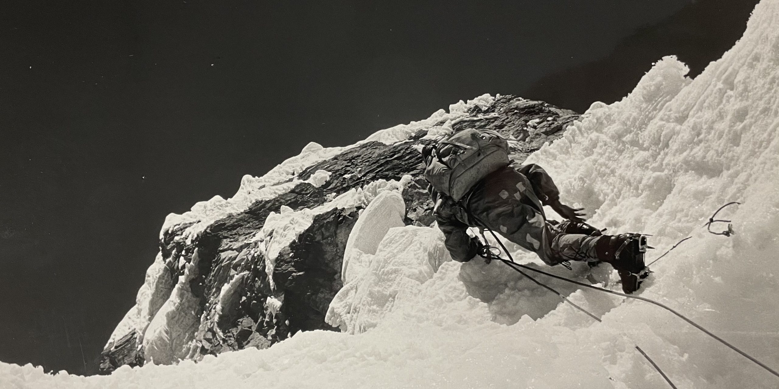 Lionnel Terray, alpiniste progressant sur une pente de glace très raide, équipé de chaussures d'alpinisme lourdes et de crampons.