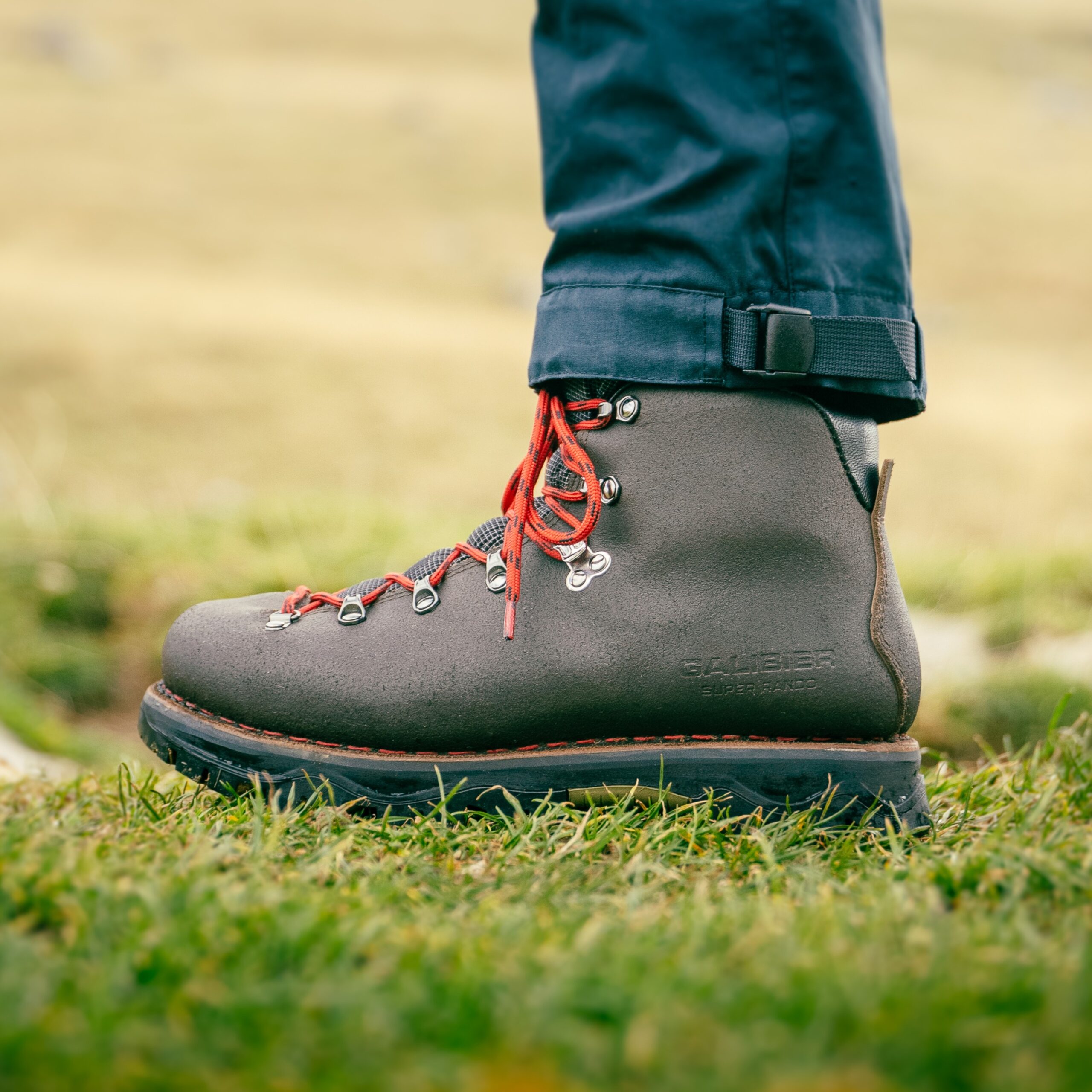 Profil de la chaussure montante femme outdoor Galibier Super Rando Mid en cuir marron avec lacets rouges sur une pelouse alpine.